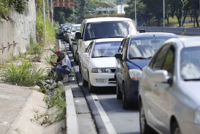 Men sit on a curb alongside vehicles lined up to enter a gas station during a nation-side fuel crunch, in Caracas, Venezuela, Wednesday, September 30, 2020. (Photo by Ariana Cubillos/AP Photo)