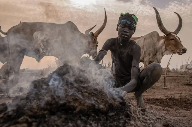 a Sudanese boy from Dinka tribe warm up by a fire in the early morning at their cattle camp in Mingkaman, Lakes State, South Sudan on March 4, 2018. (Photo by  Stefanie Glinski/AFP Photo)