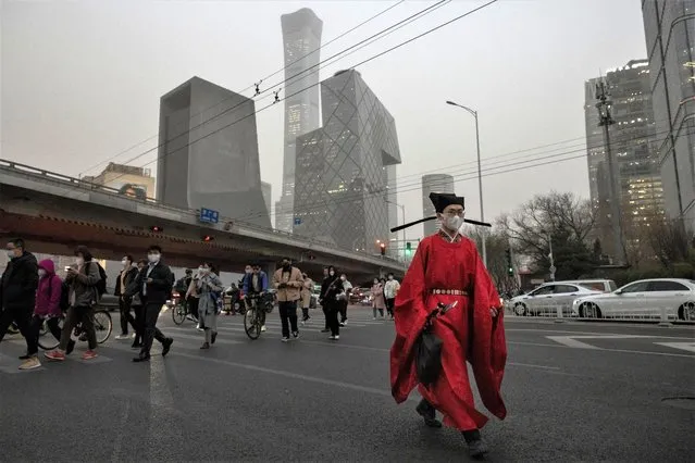 A man in a traditional costume crosses a street in the Central Business District (CBD) on a polluted day in Beijing, China on March 10, 2023. (Photo by Thomas Peter/Reuters)