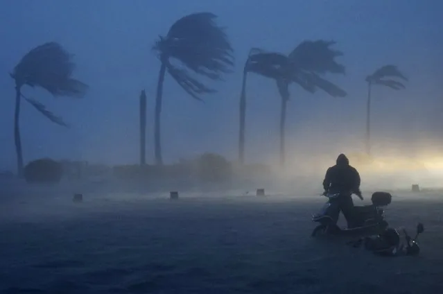 A man pushes his electric bicycle against strong wind and heavy rainfalls along a flooded seaside street as Typhoon Rammasun hits Haikou, Hainan province, China, July 18, 2014. (Photo by Reuters/Stringer)