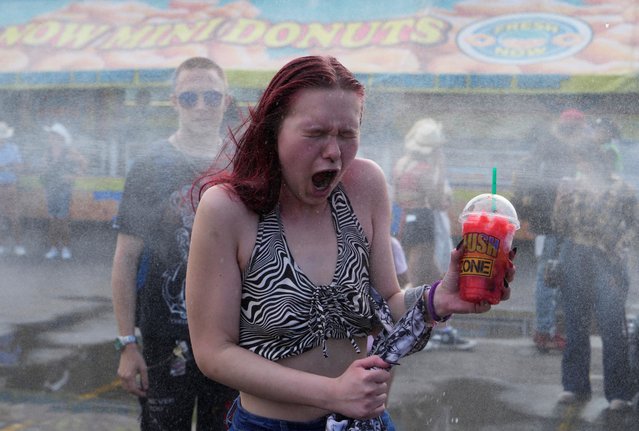 A woman reacts to cool water at a cooling station during a period of hot weather on the midway of the Calgary Stampede in Calgary, Alberta, Canada on July 8, 2024. (Photo by Todd Korol/Reuters)