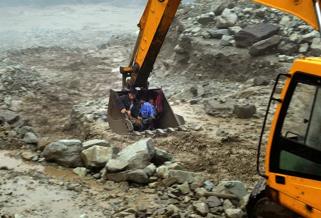 An excavator moves villagers away from a flooded area during heavy rainfall in Yingxiu, Wenchuan county, Sichuan province, July 10, 2013. More than 300 hundred people were evacuated in Yingxiu after roads connecting the township to the outside were cut off by floods and landslides. (Photo by Reuters/Stringer)