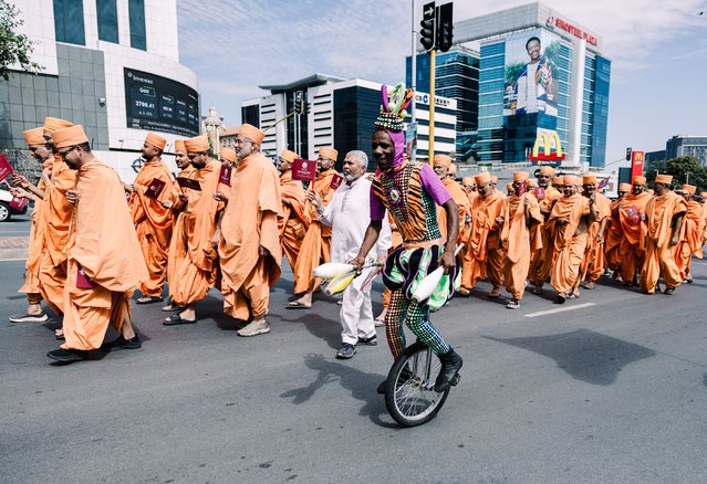 A juggler rides a unicycle past monks, or Hindu holy men, taking part in the Nagar Yatra procession in Johannesburg, on February 1, 2025. The Nagar Yatra is a lively procession of the deities on seven magnificent chariots featuring devotional music and dance ahead of the historic opening of the BAPS (Bochasanwasi Akshar Purushottam Swaminarayan Sanstha) Hindu Mandir, the largest Hindu temple and cultural complex in the Southern Hemisphere that will take place on February 2, 2025. (Photo by Rajesh Jantilal/AFP Photo)