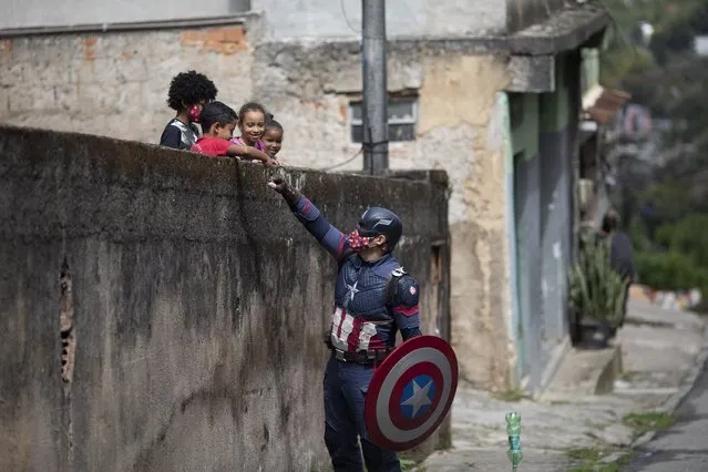 Military police officer Everaldo Pinto, dressed as superhero Captain America, greets children amid the COVID-19 pandemic in Petropolis, Rio de Janeiro state, Brazil, Thursday, April 15, 2021. Pinto advises children on the need to protect themselves against COVID-19, distributing kits equipped with cleaning products and protective face masks to prevent the spread of the new coronavirus. (Photo by Silvia Izquierdo/AP Photo)