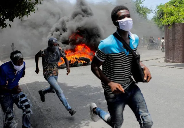 Men run next to burning tires during a protest demanding an end to gang violence, in Port-au-Prince, Haiti on August 14, 2023. (Photo by Ralph Tedy Erol/Reuters)