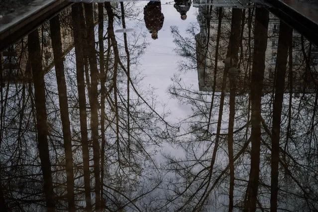 This photograph shows pedestrians reflected in a puddle on a warm spring day in Moscow on March 26, 2021. (Photo by Dimitar Dilkoff/AFP Photo)