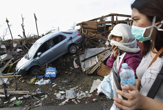 People covering their faces pass a car in debris after super typhoon Haiyan battered Tacloban City, in central Philippines November 13, 2013. Philippine officials have been overwhelmed by Haiyan, one of the strongest typhoons on record, which tore through the central Philippines on Friday and flattened Tacloban, coastal capital of Leyte province where officials had feared 10,000 people died, many drowning in a tsunami-like wall of seawater. (Photo by Edgar Su/Reuters)