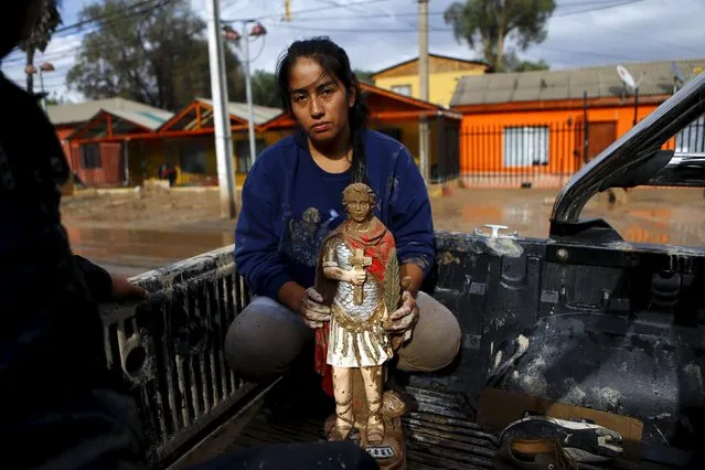 A woman holds a religious figure covered in mud as she is evacuated from her house at Copiapo city, March 26, 2015. (Photo by Ivan Alvarado/Reuters)