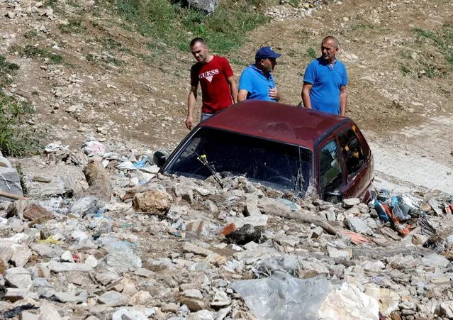 People work near a damaged car from the overnight floods in the village of Gjermo, North Macedonia on August 23, 2022. (Photo by Ognen Teofilovski/Reuters)