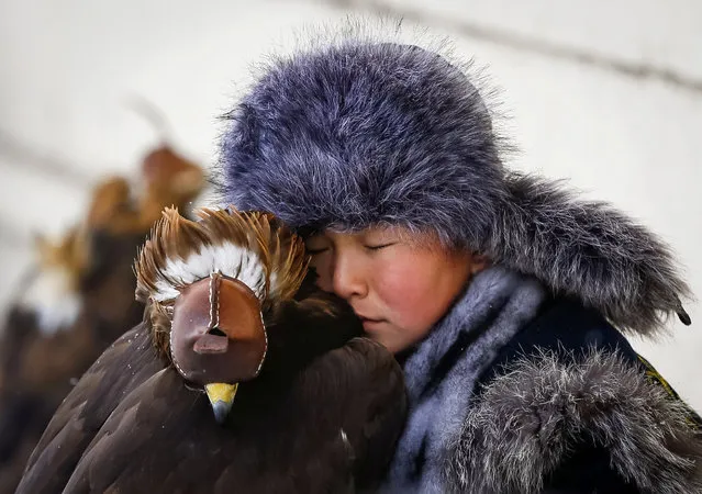 A young hunter rests next to his tamed golden eagle during an annual hunters competition at Almaty hippodrome, Kazakhstan February 9, 2018. (Photo by Shamil Zhumatov/Reuters)