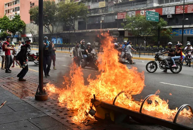 A protester burns a motorcycle during clashes with the security forces in a protest against the government of President Nicolas Maduro on the anniversary of the 1958 uprising that overthrew the military dictatorship, in Caracas on January 23, 2019. Venezuela's National Assembly head Juan Guaido declared himself the country's “acting president” on Wednesday during a mass opposition rally against leader Nicolas Maduro. (Photo by Yuri Cortéz/AFP Photo)