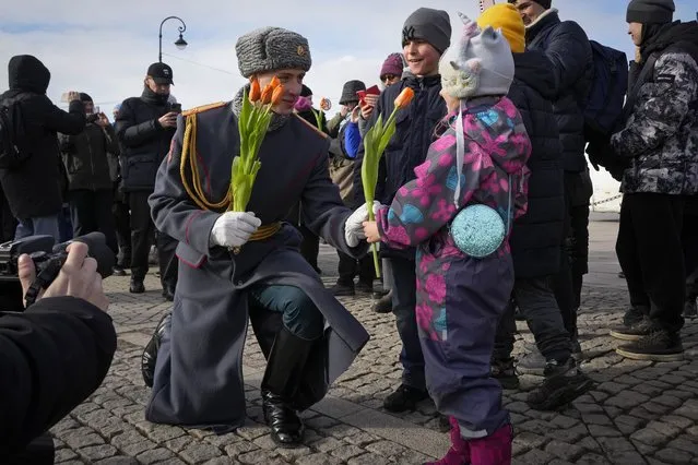 A honour guard soldier gives a flower to a girl on International Women's Day in St. Petersburg, Russia, Friday, March 8, 2024. International Women's Day on March 8 is an official holiday in Russia. Per tradition, men give flowers and gifts to female relatives, friends and colleagues, even though in the past two years flowers have gotten more expensive. Marches, demonstrations and conferences are being held the world over, from Asia to Latin America and elsewhere. (Photo by Dmitri Lovetsky/AP Photo)