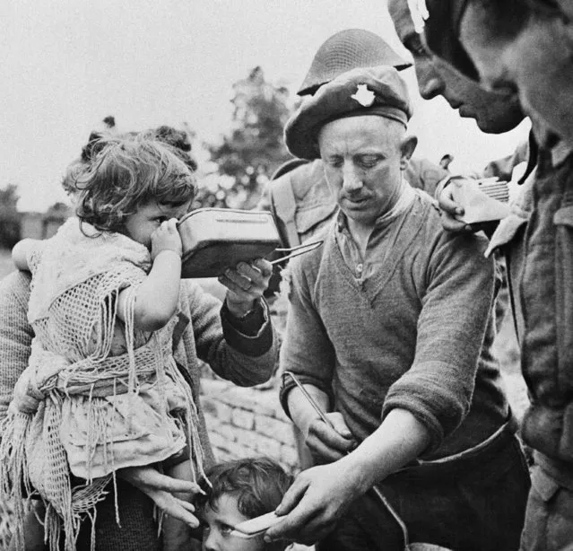 French refugees, including women and children, gather around British soldiers at a Civil Affairs Feeding Center in the Normandy beachhead sector who are supplying hot food on June 16, 1944. Many of the refugees had not eaten for three or more days. (Photo by AP Photo)