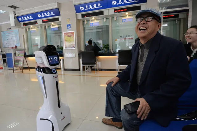 A customer laughs as he talks with a robot assistant at a branch of Bank of Communications in Handan, Hebei province, March 29, 2016. (Photo by Reuters/China Daily)