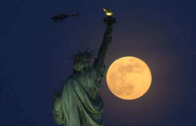 A helicopter flies past as the full moon rises behind the Statue of Liberty on May 18, 2019 in New York City. (Photo by Johannes Eisele/AFP Photo)