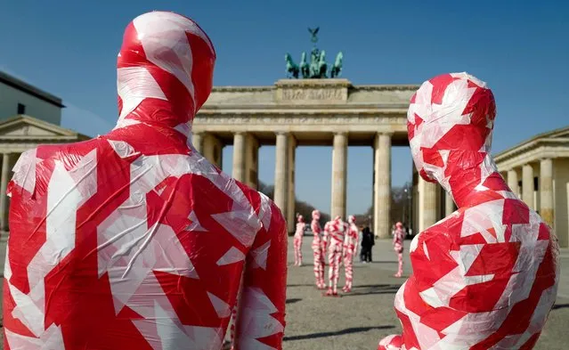 Mannequins wrapped in barrier tape stand in front of Berlin's landmark Brandenburg Gate on March 31, 2021, as part of German artist Dennis Josef Meseg's Corona Memorial called “It is Like it is”. The moving exhibition will be set up near various landmarks in the German capital over the next days. (Photo by John MacDougall/AFP Photo)