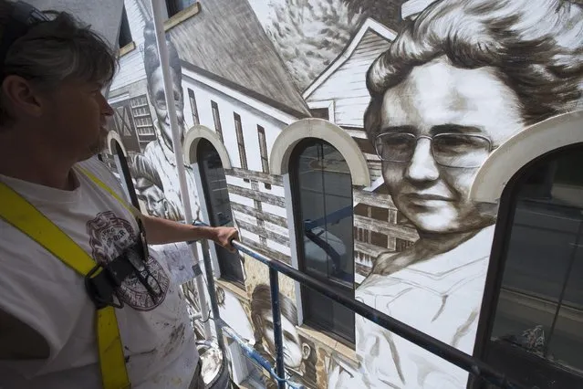 Artist Jason Morgan rides a lift as he works on a mural named "Heritage Harvesters" as commissioned by a building owner to depict farmers from the community, Thursday, June 11, 2015, in Wilmington, Ohio. Locals were asked to send photographs of their ancestors who lived in the Wilmington area to adorn the edifice that sits along the town's main drag. (AP Photo/John Minchillo)