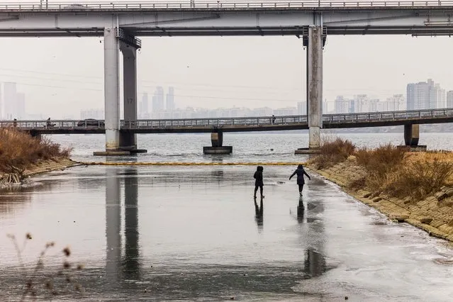People walk on a frozen section of the Han river in Seoul on December 28, 2021. (Photo by Anthony Wallace/AFP Photo)