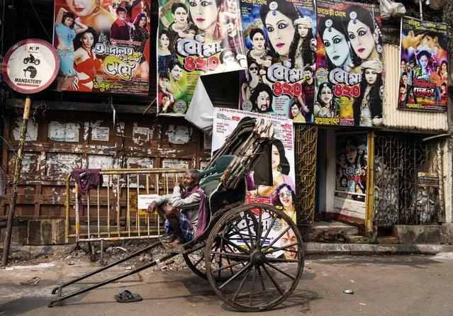 A hand rickshaw puller waits for customer in front of theatre posters pasted on wall in Kolkata, India, Wednesday, February 9, 2022. (Photo by Bikas Das/AP Photo)
