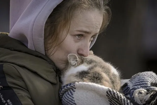 A woman who was evacuated from Irpin cries kissing a cat wrapped in a blanket at a triage point in Kyiv, Ukraine, Friday, March 11, 2022. (Photo by Vadim Ghirda/AP Photo)