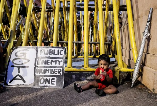 A baby holds a packet of biscuits as he sits in front of the metal barrier at the Presidential Secretariat during a protest against Sri Lanka President Gotabaya Rajapaksa, amid the country's economic crisis in Colombo, Sri Lanka, April 11, 2022. (Photo by Dinuka Liyanawatte/Reuters)