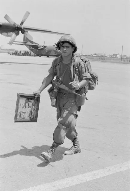 A U.S. soldier, carrying a portrait of himself and his girlfriend, walks across the Phu Bai Air Base, June 27, 1972, as he starts his trip back to the United States.  Most of his unit, the 196th Brigade, is being returned to the U.S. (Photo by Peter Winterbach/AP Photo)