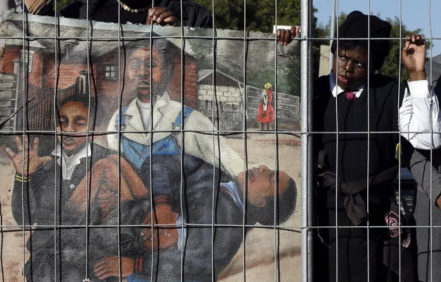 A young girl watches the laying of the wreath ceremony, at the Hector Pieterson Memorial, in Soweto, South Africa, Thursday, June 16, 2016, near to a painting depicting the iconic photo showing 13-year-old Hector Pieterson, being carried after being shot by police during the 1976 Soweto uprising, displayed by an artist for commemoration of the 40th anniversary of uprisings. South Africans are commemorating the 40th anniversary of a pivotal moment in the anti-apartheid struggle, a 1976 black student uprising in the Soweto area of Johannesburg that led to a deadly crackdown but launched a new phase of opposition to white minority rule. (Photo by Themba Hadebe/AP Photo)