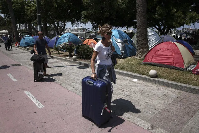 Tourists make their way past tents where migrants have set up on a square of Kos town on the southeastern island of Kos, Monday, August 10, 2015. (Photo by Yorgos Karahalis/AP Photo)