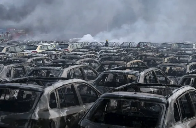 A firefighter works at the site near damaged vehicles as smoke rises from the debris after the explosions at the Binhai new district in Tianjin, China, August 13, 2015. (Photo by Reuters/China Daily)