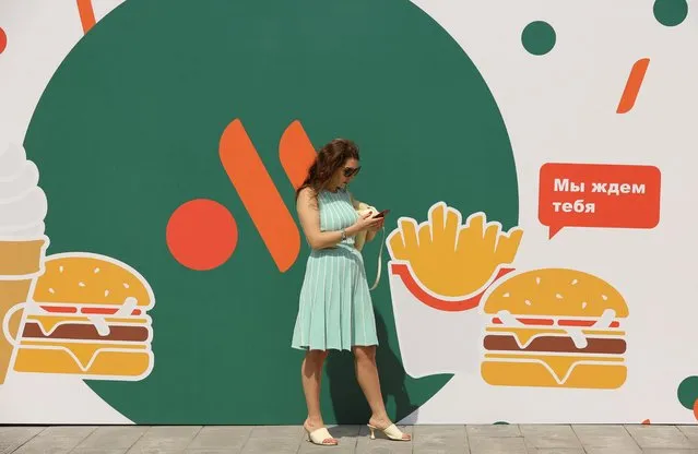 A woman stands next to a banner before the opening of the new restaurant “Vkusno & tochka” following McDonald's Corp company's exit from the Russian market in Moscow, Russia on June 12, 2022. (Photo by Evgenia Novozhenina/Reuters)