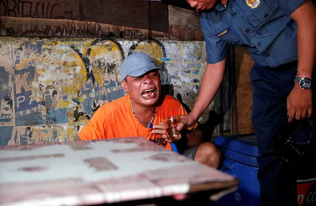 A police officer gives a glass of water to a man as he comforts him after his brother, who police say was killed in a spate of drug-related violence overnight, was shot in Manila, Philippines on August 17, 2017. (Photo by Dondi Tawatao/Reuters)