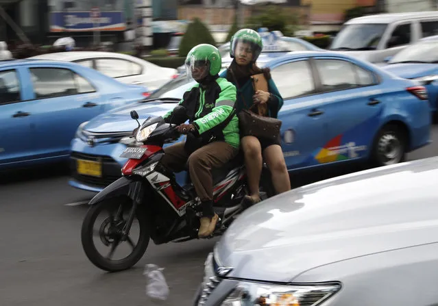 In this Friday, April 29, 2016, a driver of GrabBike, a direct competitor of the motorcycle taxi app Go-Jek, rides with a customer through traffic in Jakarta, Indonesia. Motor cycle ride-hailing apps are now part of daily life in the city that is known for having the world's worst traffic. (Photo by Tatan Syuflana/AP Photo)