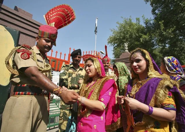 An Indian woman ties a “Rakhi” or a traditional Indian sacred thread onto the wrist of Indian Border Security Force (BSF) soldier during the Raksha Bandhan celebrations at the India-Pakistan joint check post at the Wagah border on the outskirts of Amritsar, India, August 29, 2015. (Photo by Munish Sharma/Reuters)