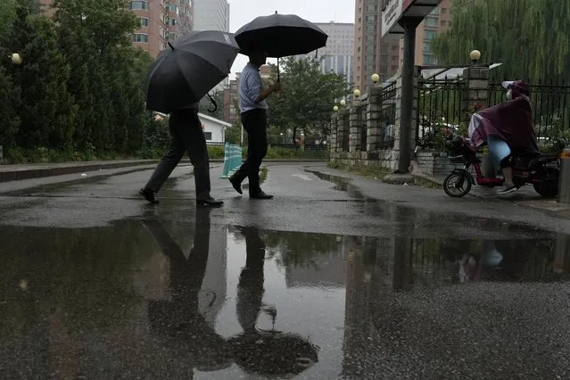 Residents walk with umbrellas near a puddle during a rainy day in Beijing, Thursday, August 18, 2022. (Photo by Ng Han Guan/AP Photo)