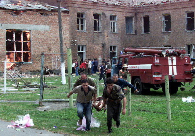 Volunteers carry an injured civilian to safety while soldiers stormed a school seized by heavily armed masked men and women in the town of Beslan in the province of North Ossetia near Chechnya , September 3, 2004. A hundred or more people were killed when Russian troops stormed a school on Friday in a chaotic battle to free parents, teachers and children who had been held hostage for 53 hours by Chechen separatists. (Photo by Reuters/Stringer)