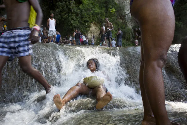 In this July 16, 2016 photo, a Voodoo pilgrim holds a bowl that has her name written on it, as she bathes in a waterfall believed to have purifying powers during the annual celebration in Saut d' Eau, Haiti. Pilgrims ask favors of the Virgin Our Lady of Carmel or the Voodoo diety Erzulie. (Photo by Dieu Nalio Chery/AP Photo)