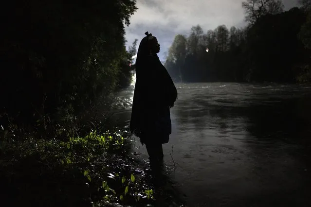 Millaray Huichalaf, a Mapuche machi, or healer and spiritual guide, poses for a portrait in the Pilmaiquen River silhouetted by lights from the construction site of a hydroelectric plant in Carimallin, southern Chile, on Monday, June 27, 2022. Huichalaf has led a sometimes-violent battle against hydroelectric plants on the Pilmaiquen, which flows through rolling pastures from a lake in the Andean foothills. (Photo by Rodrigo Abd/AP Photo)