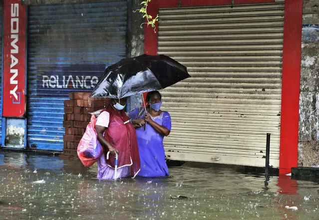 People wearing masks as a precaution against the coronavirus try to make their way through a water logged street during heavy rain in Mumbai, India, Tuesday, August 4, 2020. India's monsoon season runs from June to September. (Photo by Rajanish Kakade/AP Photo)
