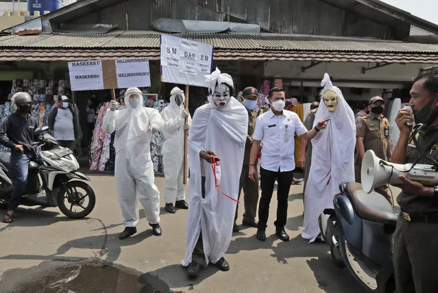 Government officials dressed as a shrouded ghosts, traditionally known as a “pocong”, to represent the victims of COVID-19, take part in a coronavirus awareness campaign at a market in Tangerang, Indonesia, Wednesday, September 16, 2020. Writings on the posters read “My mask protects you, your mask protects me” and “Wear mask, wash your hands, keep your distance”. (Photo by Tatan Syuflana/AP Photo)