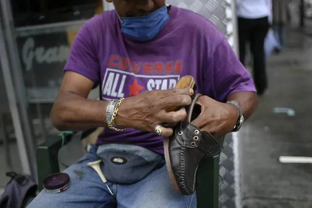 A shoeshiner, wearing a protective face mask, brushes a shoe on Sabana Grande boulevard in Caracas, Venezuela, Saturday, August 1, 2020, amid the new coronavirus pandemic. (Photo by Matias Delacroix/AP Photo)