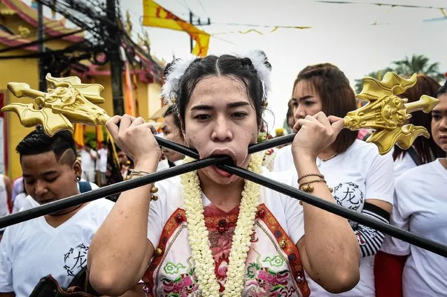A devotee of the Nine Emperor Gods marches with large poles pierced through her cheeks during the annual Phuket Vegetarian Festival in the southern province of Phuket on October 1, 2016. Swords, axe handles, kebab skewers and even a model boat were just some of the objects placed in devotees' pierced cheeks as southern Thailand's gruesome vegetarian festival got under way. (Photo by Lillian Suwanrumpha/AFP Photo)