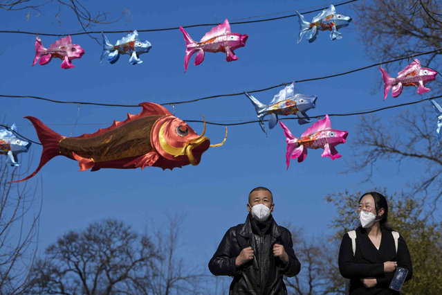 People wearing face masks walk under fish shaped lanterns on display in a green space in Beijing, Monday, February 20, 2023. (Photo by Andy Wong/AP Photo)