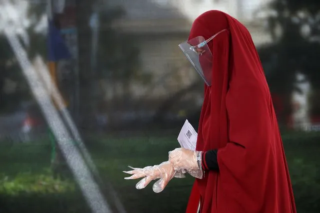A voter wearing a protective mask and a protective shield adjusts her gloves during regional elections in Tangerang, near Jakarta, Indonesia on December 9, 2020. (Photo by Willy Kurniawan/Reuters)