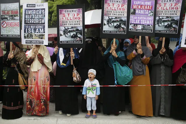 A child infront of protesters from Hizbut Tahrir Malaysia Islamic group holding placards during a protest in front of the US embassy in Kuala Lumpur, Malaysia, 13 November 2015. Hizbut Tahrir Malaysia labelled Obama as an 'enemy' of Islam, citing the deaths of Muslims in Iraq, Afghanistan, as well as in the ongoing Syrian conflict, which they blame on the US President’s administration. (Photo by Fazry Ismail/EPA)