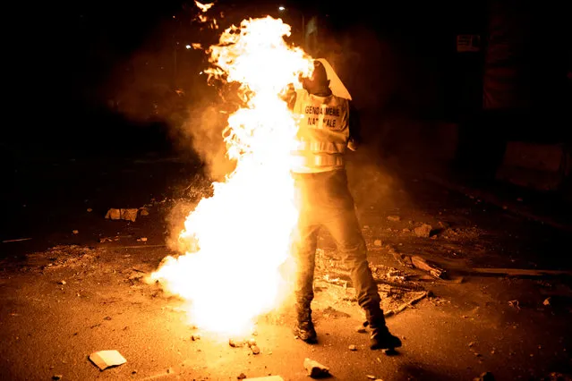 A Senegalese police gets covered in flames as he tries to put-out a fire, after protests erupted during a curfew in Dakar on January 6, 2021. Senegalese President Macky Sall announced on the evening on January 6 the state of emergency with a night curfew for two regions including Dakar to stop the rise of the coronavirus. (Photo by John Wessels/AFP Photo)