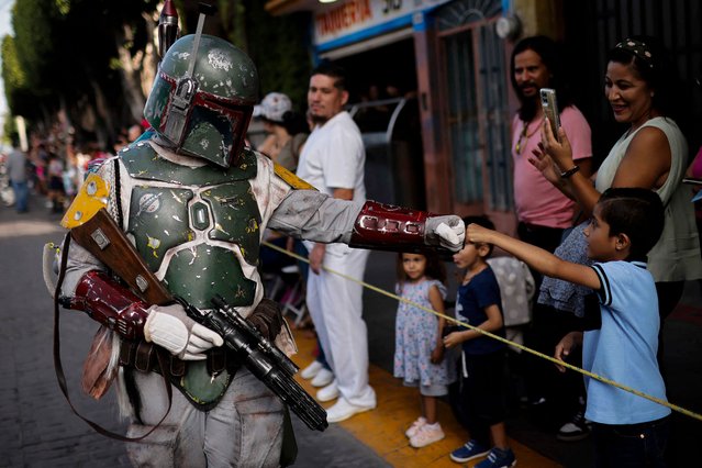 A fan of the Star Wars saga fancy dressed as a character greets with a fist bumb to a kid during the so-called “Training Day” parade at Los Heroes Avenue in Leon, Guanajuato State, Mexico, on August 10, 2024. (Photo by Rodrigo Oropeza/AFP Photo)