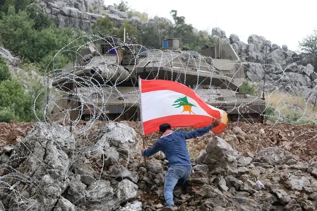 A Lebanese protester plants the national flag across the fence from an Israeli tank during an anti-Israeli demonstration near the “blue line” area, a demarcation line drawn by the UN to mark Israel's withdrawal from southern Lebanon in 2000, near the Lebanese southern village of Kfar Shuba on June 9, 2023. (Photo by Mahmoud Zayyat/AFP Photo)