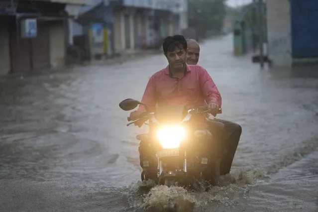 A motorcyclist wades through a flooded street following heavy winds and incessant rains after landfall of cyclone Biparjoy at Mandvi in Kutch district of Western Indian state of Gujarat, Friday, June 16, 2023. Cyclone Biparjoy knocked out power and threw shipping containers into the sea in western India on Friday before aiming its lashing winds and rain at part of Pakistan that suffered devastating floods last year. (Photo by Ajit Solanki/AP Photo)