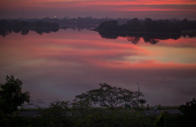 People walk on a path along a lake mirrored with clouds after sunset in Yangon, Myanmar, Wednesday, January 6, 2016. (Photo by Gemunu Amarasinghe/AP Photo)