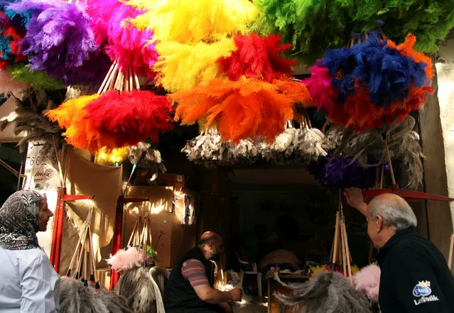 People stand under coloured ostrich feather dusters hanging in a shop in Beirut, Lebanon May 2, 2016. (Photo by Alia Haju/Reuters)